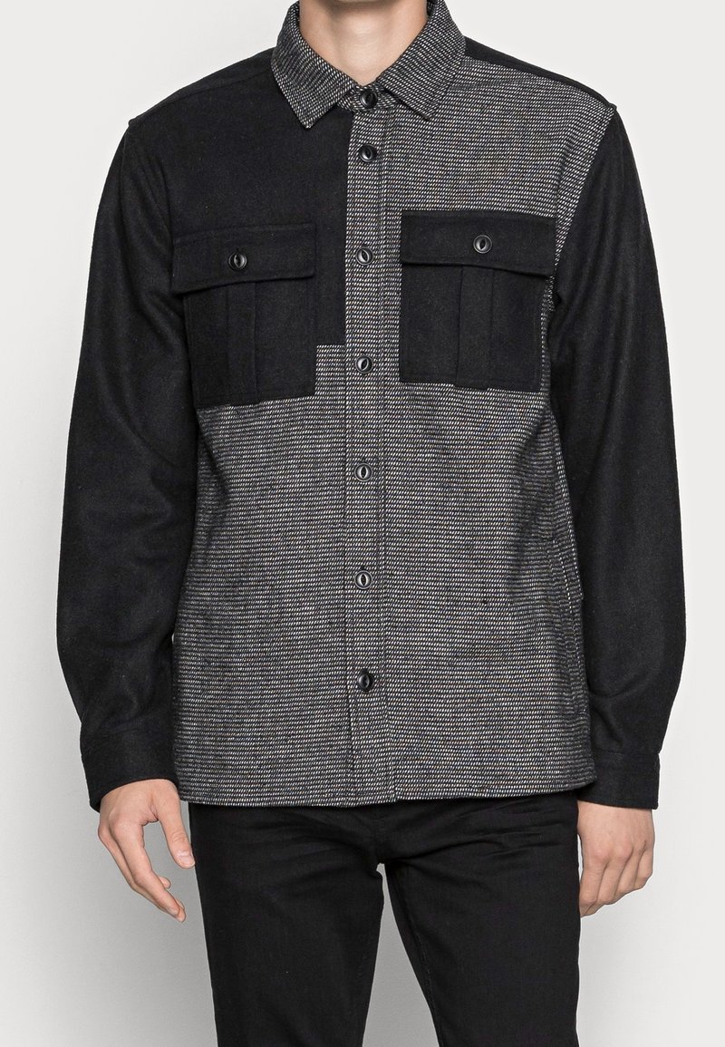Sort og gråternet flannel skjorte med knaplukning, brystlommer og kontraststoffpaneler. Blød tekstur, skræddersyet design.