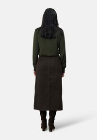 Groene lange mouw top gecombineerd met een bruine ribbel midi-rok, met een rechte snit en zijnaaddetails. Bruine hoge hakken worden gedragen.