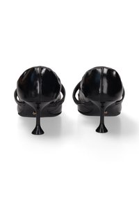 Chaussures à talons hauts en cuir noir au design épuré, avec un dos courbé et un fin talon aiguille. Texture lisse et polie avec des accents minimaux.