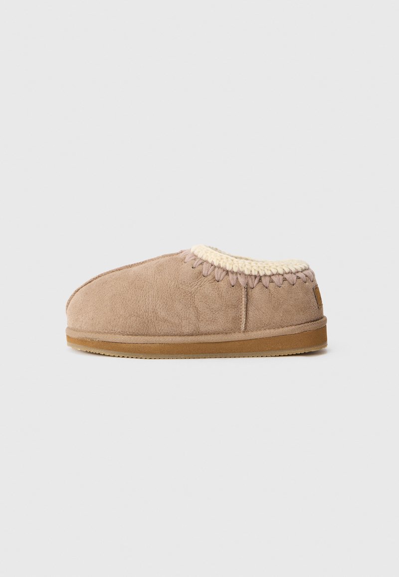 Beige mockasiner i mockaskinn med krämfärgad stickad kant, låg klack och brun gummisula, visade på en enkel vit bakgrund.