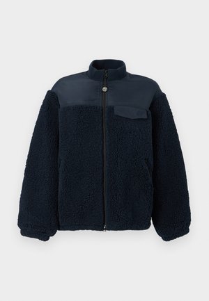 Jachetă din fleece albastru marin cu fermoar integral frontal, guler înalt, buzunare laterale cu fermoar și un buzunar cu clapetă pe piept, pe partea stângă.