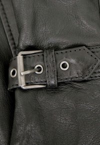 Close-up of a black leather strap with metal buckle and stitching on a leather garment.