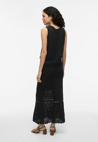 Ensemble en deux pièces en crochet noir comprenant un top sans manches et une jupe longue. La texture est à trame ouverte, avec des bords en forme de vagues à l'ourlet.