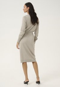 Robe midi grise claire à manches longues avec une taille ceinturée et des poignets côtelés, confectionnée en tissu doux et texturé. Design simple et épuré.