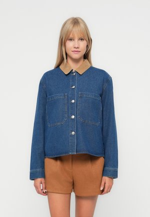 Korte spijkerjack met een tan corduroy kraag, twee voorkze pockets, knoopsluiting en een medium blauwe wassing. Glad textuur.