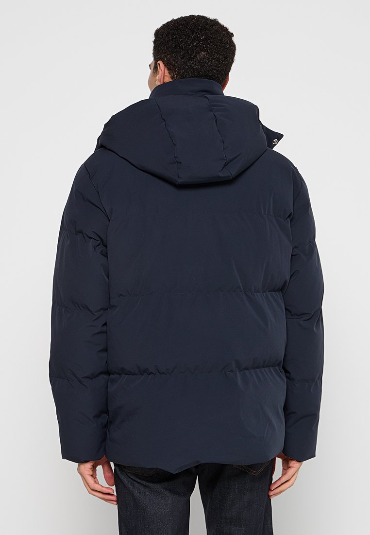 Navy pufferjack met capuchon, met een gequilt ontwerp en een gestroomlijnde silhouet. Het materiaal is glad met een matte afwerking.