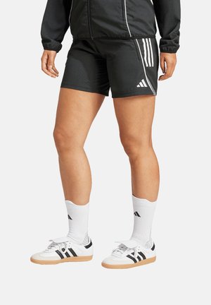 Zwarte sportshorts met witte accenten en drie strepen. Gecombineerd met witte schoenen met zwarte strepen en witte sokken.