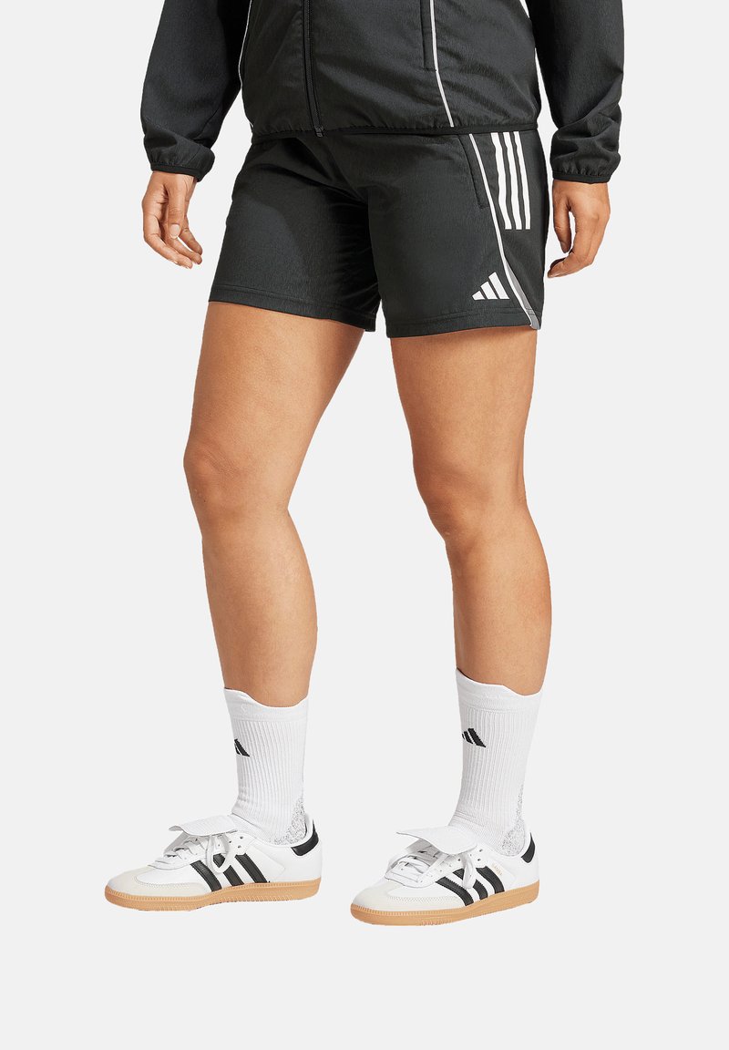 Zwarte sportshorts met witte accenten en drie strepen. Gecombineerd met witte schoenen met zwarte strepen en witte sokken.