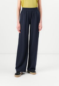 Navy wide-leg trousers with an elastic waistband, made of a smooth fabric. Paired with a short-sleeve yellow top and black sneakers.
