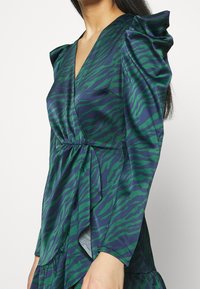 Green and navy tiger-striped dress with puffed sleeves, V-neckline, cinched waist, and flowing skirt, made from smooth fabric.