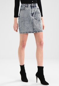 Minifalda de mezclilla en gris azulado deslavado, con cintura ajustada, diseño de cinco bolsillos y dobladillo deshilachado sutil. Combinada con botas de tobillo negras de tacón.