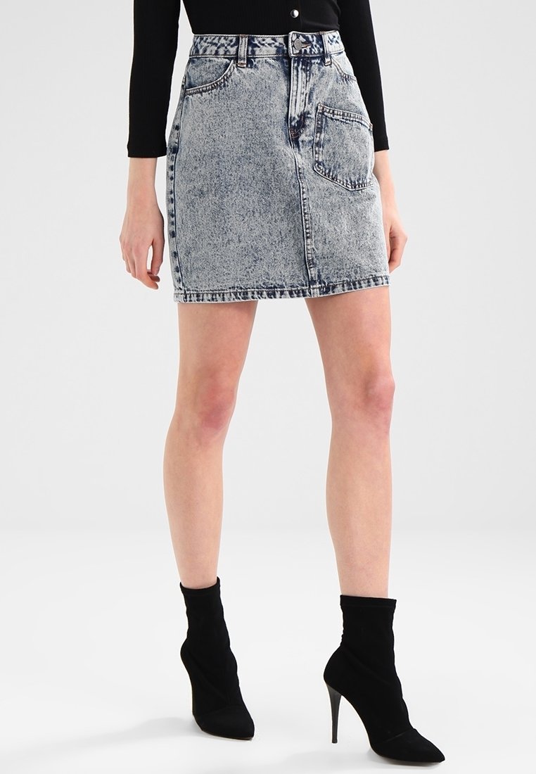 Minifalda de mezclilla en gris azulado deslavado, con cintura ajustada, diseño de cinco bolsillos y dobladillo deshilachado sutil. Combinada con botas de tobillo negras de tacón.