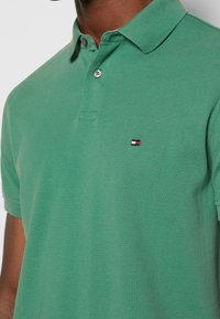 Green polo shirt made of textured cotton, featuring a two-button placket, short sleeves, and a small logo in red, white, and blue on the chest.