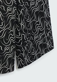 Černá tkanina s bílým vlnitým vzorem. Design je abstraktní a textura hladká. Okraj oděvu je upravený pečlivě.