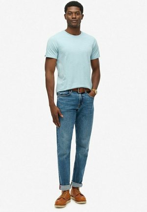Camiseta de algodón de color azul claro combinada con unos vaqueros ajustados azules. Zapatos marrones con cordones y puños doblados. Elementos de diseño simples, casuales y modernos.