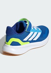 Blauer Sportschuh mit einer strukturierten Mesh-Oberfläche, weißen Akzenten, einem grünen Ferselement und einer weißen Gummisohle mit Grip.
