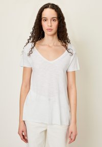 Bijela majica kratkih rukava s V izrezom od lagane tkanine s opuštenim krojem. Mekana tekstura, pomalo prozirna, rub pada do bokova.