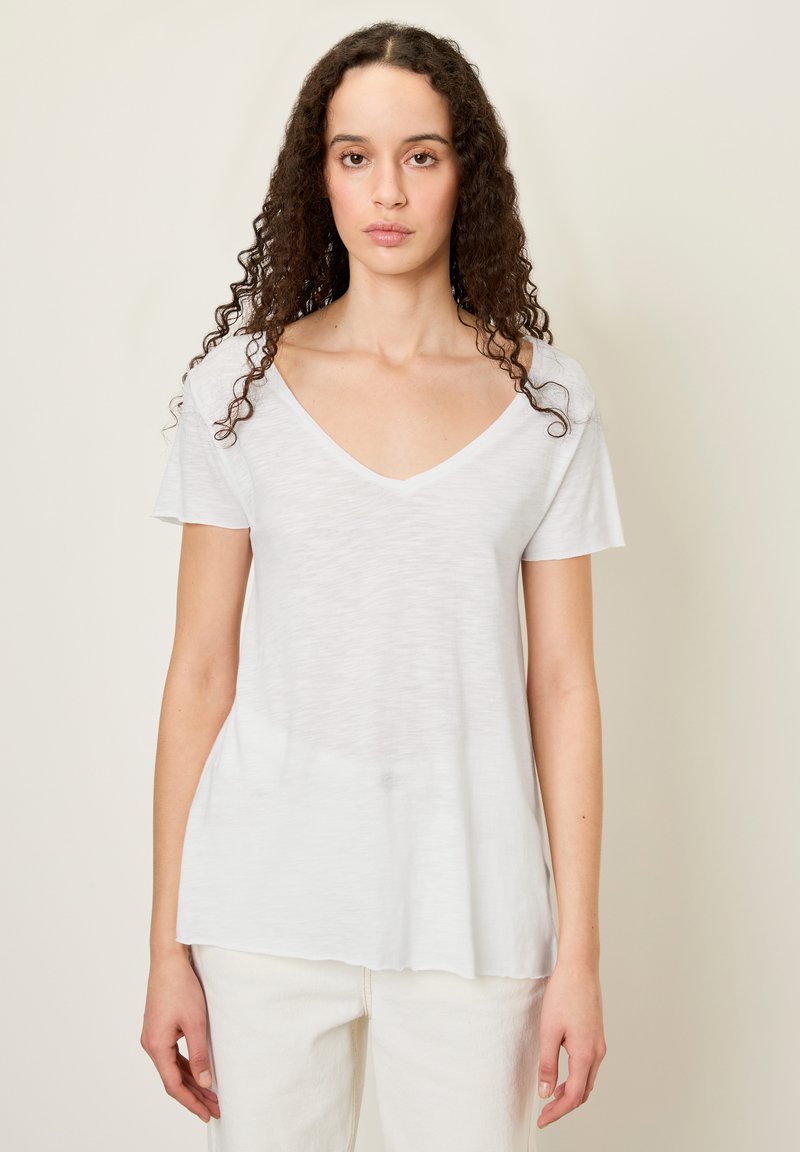 Bijela majica kratkih rukava s V izrezom od lagane tkanine s opuštenim krojem. Mekana tekstura, pomalo prozirna, rub pada do bokova.