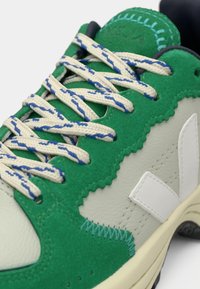 Rohelisest seemisnahast ja valgest nahast vabaajajalanõu, millel on tekstuuriga detailid, punutud paelad siniste niitidega ja kihiline disain.