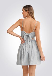 Gestreepte jurk met een aansluitend bovenlijf en een open rug. Heeft dunne bandjes en een strikdetail in de taille. Rok is volumineus en knielang.