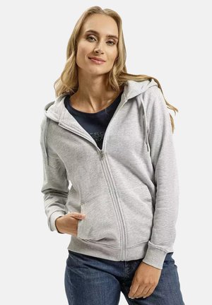 Szary hoodie na zamek z miękką teksturą, przednimi kieszeniami, regulowanym kapturem i luźnym krojem, w zestawie z granatową koszulką i dżinsami.