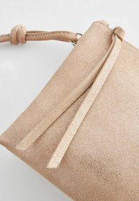Svetlohnedá clutch kabelka z falošnej semišovej kože s textúrovaným povrchom, vybavená uzlom na popruhu a zipsom, doplnená hladkým, lesklým okrajom.