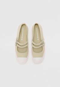 Chaussures en toile beige avec deux sangles ajustables et des accents roses, dotées d'un embout en caoutchouc blanc et d'une semelle texturée pour une meilleure adhérence.