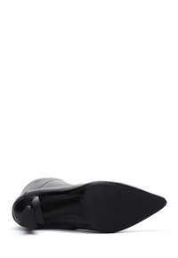 Stivaletto in pelle nera con punta affusolata, texture liscia, dettagli di cucitura sottile e tacco basso e arrotondato. La suola è piatta e in gomma.