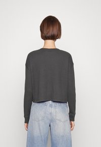 Maglione grigio a coste con maniche lunghe e un design cropped, abbinato a jeans a vita alta di colore blu chiaro. Tessuto semplice e strutturato.