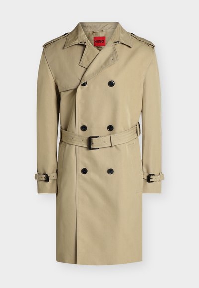 Trench-coat beige croisé avec boutons noirs, épaulettes, ceinture à la taille et aux poignets, présenté sur fond blanc.