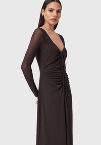 Schwarzes langärmliges Kleid aus glattem Material mit tiefem V-Ausschnitt, gerafften Details vorne und Kordelzügen als Akzente.