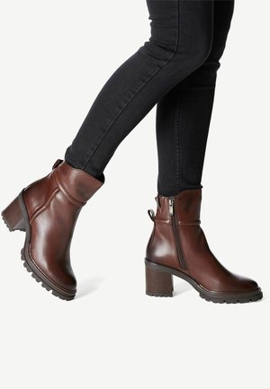 Bruine leren enkelboots met een chunky hak, een zijrits, een gestructureerde zool en een strak ontwerp, gecombineerd met zwarte slim-fit jeans.