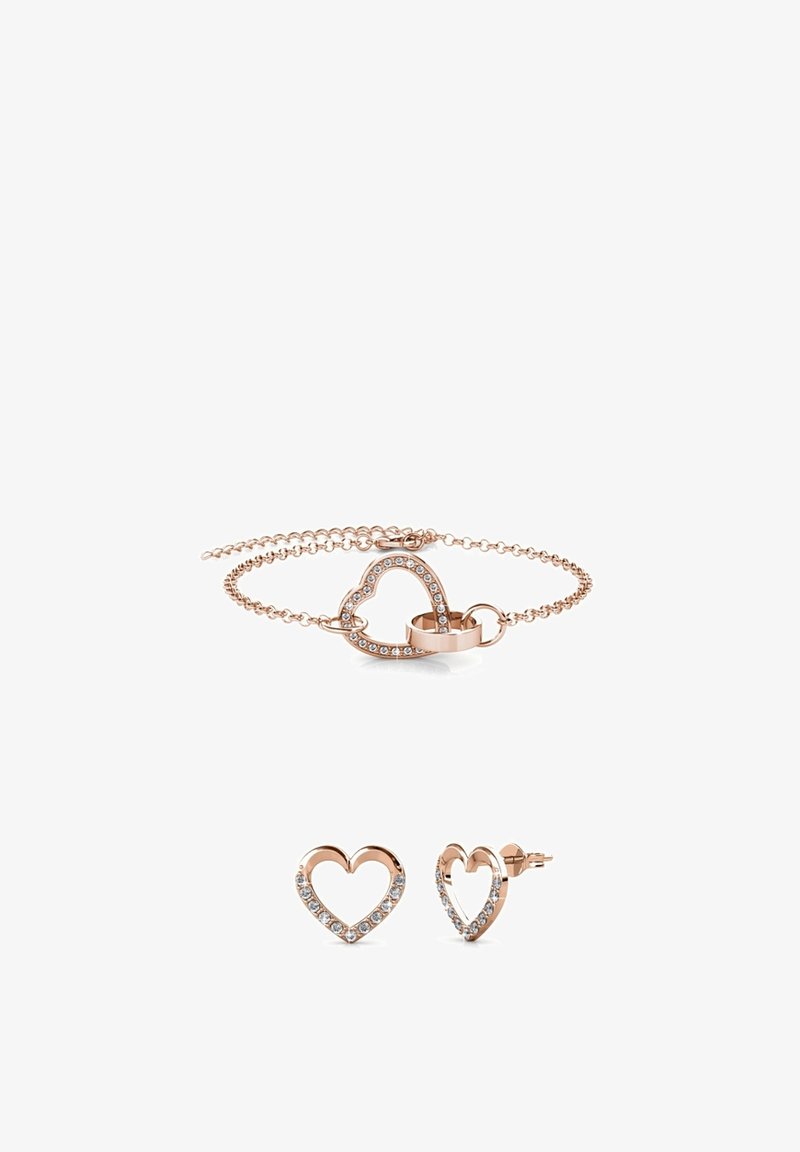 Set di gioielli in oro rosa composto da un bracciale a forma di cuore con gemme trasparenti e orecchini a bottone a forma di cuore coordinati. Finitura metallica liscia, catena delicata.