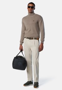 Maglione a collo alto beige, pantaloni beige chiaro, borsa a tracolla nera con logo e scarpe da ginnastica nere con dettagli marroni. Tessuto dalla texture liscia.