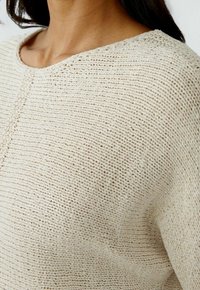 Maglione lavorato a maglia beige con scollo rotondo, caratterizzato da un modello a righe testurizzato e una vestibilità rilassata, realizzato in un tessuto morbido e traspirante.