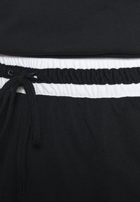 Shorts deportivos negros con una cinturilla elástica blanca, que cuentan con cordón y textura acanalada. Detalle en primer plano de la tela.