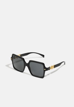 Óculos de sol grandes e pretos com lentes quadradas, detalhes em dourado nas hastes e um acabamento brilhante. Apresenta duas finas linhas horizontais douradas na armação.