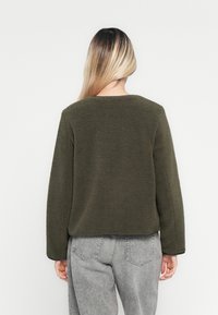 Olivenfarget fleecegenser med teksturert overflate, rund halslinning og lange ermer. Kortsiktig design med svart kant på kanten.