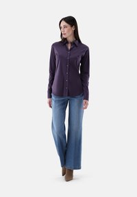 Lila langärmliges Hemd mit knöpfbarem Design, kombiniert mit hellblauen weiten Jeans und beigen spitzen High Heels.
