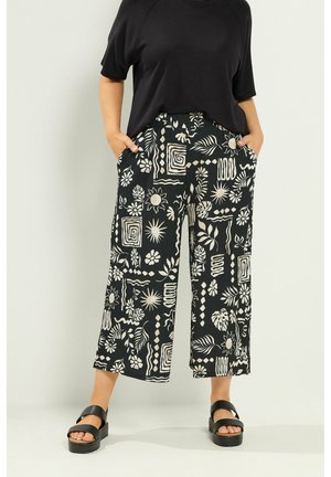 Mujer que lleva pantalones cortos negros con patrones florales y geométricos blancos, combinados con una camiseta negra y sandalias negras de plataforma.