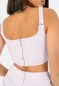 Top corto a coste lilac con spalline regolabili e dettagli con zip al centro sul retro. Il tessuto è testurizzato e aderente, complementando il design.