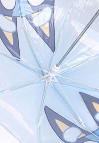 Lichtblauwe paraplu met een transparante canopy, versierd met donkerblauwe en beige accentpatronen die lijken op dierengezichten. Witte spaken en metalen handvat.