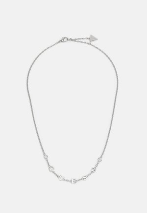 Collier chaîne fine en argent avec des lettres formant "GUESS" et des accents en cristal ronds sur fond blanc.