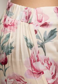 Fustă florală cu talie elastică și adunată. Prezintă modele mari de bujori roz și roșu pe un fundal bej deschis. Textură netedă.