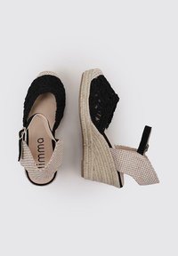 Sandales compensées avec un dessus texturé noir, des brides à carreaux beiges et une semelle en jute tissée. Sangle de cheville ajustable pour un maintien sécurisé.