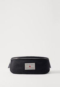 Schwarze Nylon-Tasche mit runder Form, ausgestattet mit einer silbernen Logo-Plakette und einem Reißverschluss. Enthält eine Schlaufe an der Seite für einfaches Tragen.