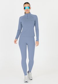 Ljusblått sportkläder med en dragkedjeförsedd långärmad topp och åtsittande leggings, kombinerat med metalliska silverskor och reflektorbrillor.