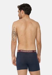 Námořnické modré boxerky s vínovým elastickým pasem označeným "DANISHRANCE", které se vyznačují těsným střihem a hladkým povrchem.