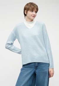 Svijetloplava, rebrasta pletena majica s V-izrezom i spuštenim ramenima, u kombinaciji s širokim plavim trapericama. Mekan materijal i opušteni kroj.