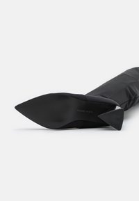 Botín negro de punta afilada y diseño elegante. Confeccionado en un material suave, presenta un tacón cónico y una suela texturizada para mayor agarre.